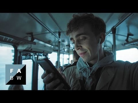 corporate video screenshot, young man standing in a bus watching smartphone wearing white earphones