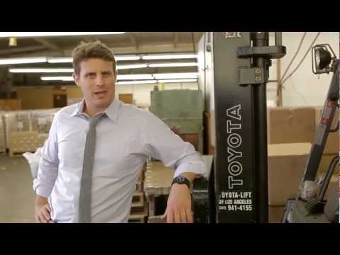 video screenshot - laid-back business man in a warehouse, watching the camera, talking with a elbow resting on a  pallet truck